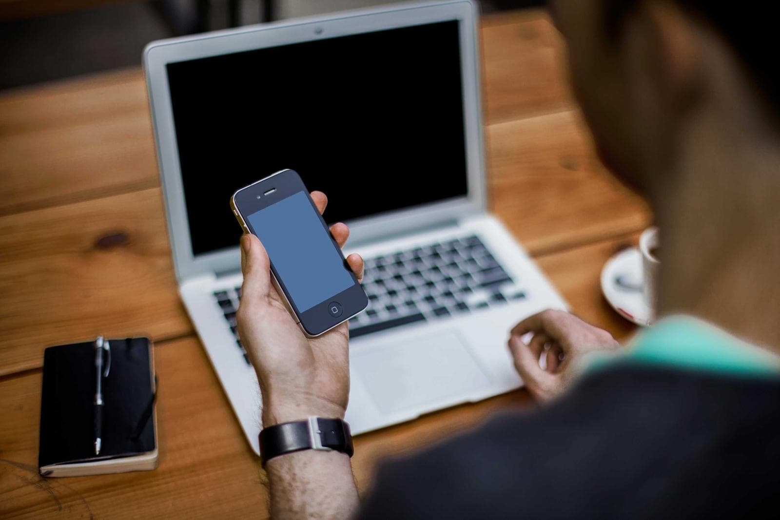Person using a laptop while holding a smartphone